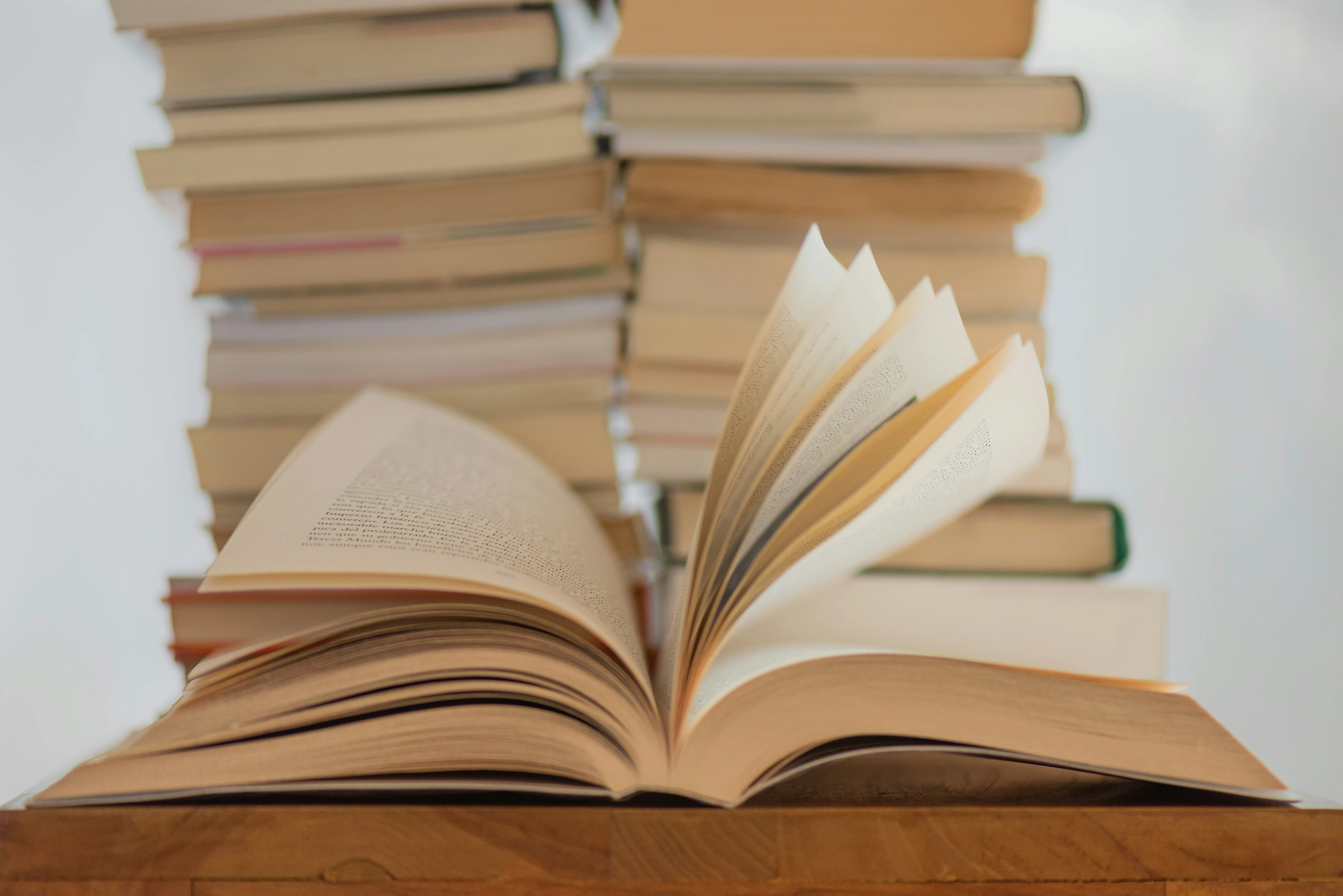 Open book with flipped pages in front of tall stacks of books.